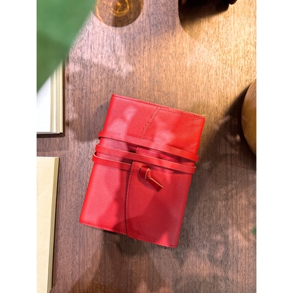 Rotes Ledernotizbuch, auf einem Holztisch liegend, mit geschlossenem Bändchen.