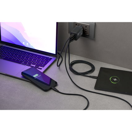 Ladegerät mit angeschlossenen Geräten, Laptop und Smartphone auf einem Tisch, Kabel verbunden.