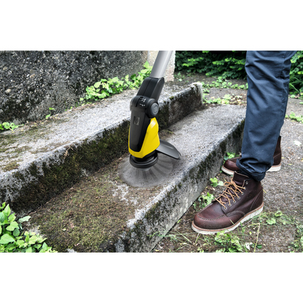 Person entfernt Unkraut mit Akku-Unkrautentferner auf einer betonierten Treppe.