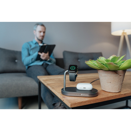Induktionsladegerät in Nutzung mit Smartwatch und Ohrstöpseln auf einem Tisch vor einer Person.