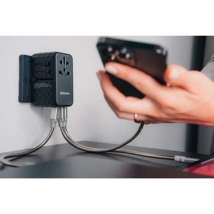 Universeller Reiseadapter mit Smartphone, an einer Wandsteckdose angeschlossen.