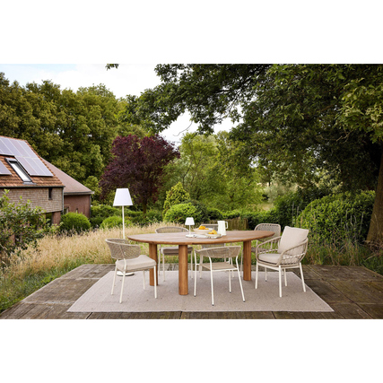 Ovaler Gartentisch aus Teak-Optik mit Stühlen in einem Gartenumfeld.