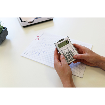 Hände halten einen Taschenrechner über einem karierten Notizblatt auf einem Tisch.