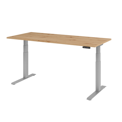 Schreibtisch in Asteiche mit silbernen Standfüßen und Bedienteil an der rechten Seite.