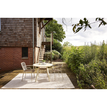 Gartenstuhl Ives aus Sand mit Aluminiumrahmen steht auf einer Terrasse neben einem runden Tisch.