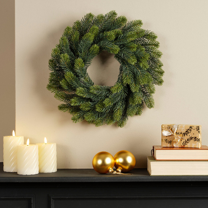 Künstlicher Weihnachtskranz in grün, an einer Wand hängen, mit Dekorationen darunter.
