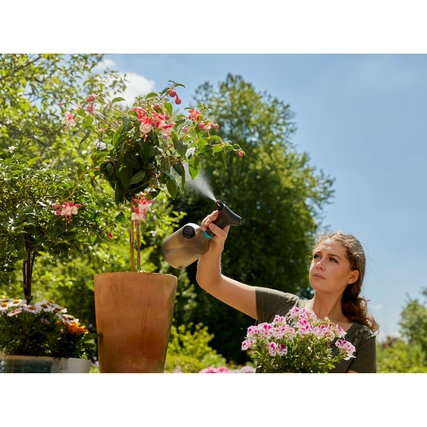 Frau besprüht mit einer Sprühflasche Pflanzen in einem Garten.