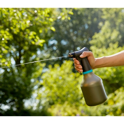 Eine Hand hält einen Pumpsprüher im Garten, während Wasser in einem Strahl sprüht.