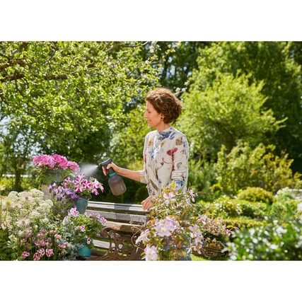 Frau mit einer Sprühflasche bewässert Blumen im Garten.