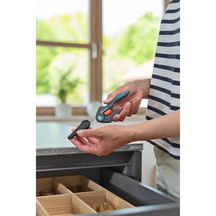 Gartenschere in Händen einer Person, die die Schutzkappe abnimmt, in heller Innenraumumgebung.