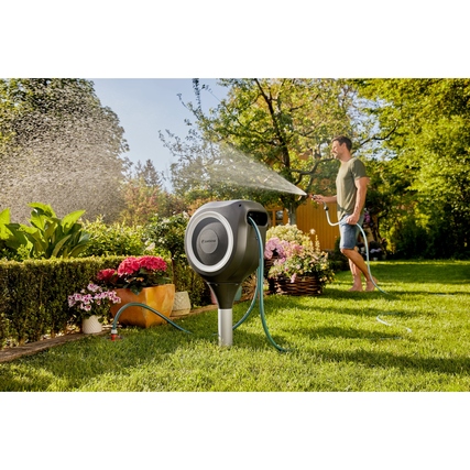 GARDENA Schlauchaufroller RollUp M steht im Garten, während ein Mann Pflanzen bewässert.