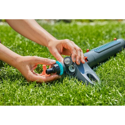Hand hält einen Anschluss des GARDENA Rasensprengers AquaZoom L auf grünem Gras.