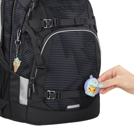 Schulrucksack mit bunten Anhängern und einem abnehmbaren Patch in der Hand.