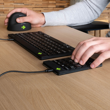 Zahlenblock mit Maus und Tastatur auf einem Tisch, Hände bedienen das Numpad.