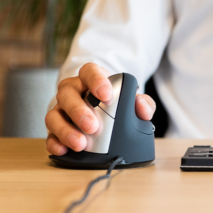 Eine Person hält eine ergonomische vertikale Maus mit Kabel an einem Schreibtisch.