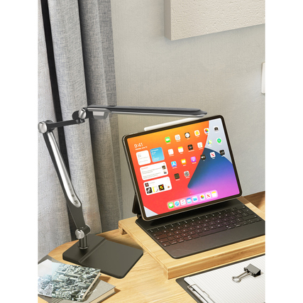 Schwarze Tischleuchte mit Gelenkarm und iPad auf einem Schreibtisch vor Vorhängen.