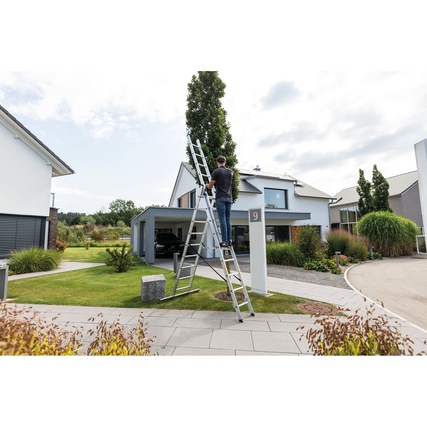 Eine Person steht auf einer dreiteiligen Multifunktionsleiter vor einem modernen Haus.