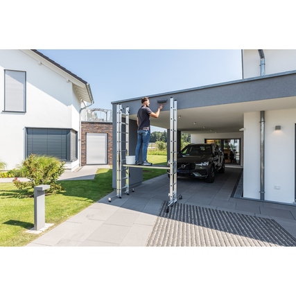 Multifunktionsleiter in Nutzung bei der Arbeit an einem Vordach, Gebäudeumgebung im Hintergrund.