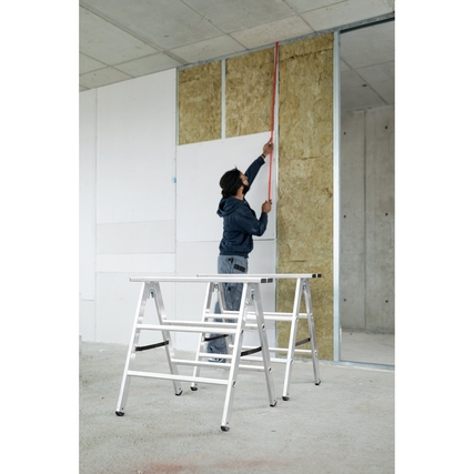 Klappbarer Arbeitsbock mit einem Handwerker beim Messen einer Wand in einem Rohbau.