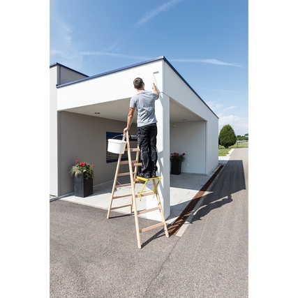 Ein Mann streicht eine Wand mit einer Holzstehleiter, während er einen Eimer in der Hand hält.