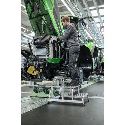 Arbeiter steht auf einer Podestleiter und wartet an einem Traktormotor in einer Werkstatt.