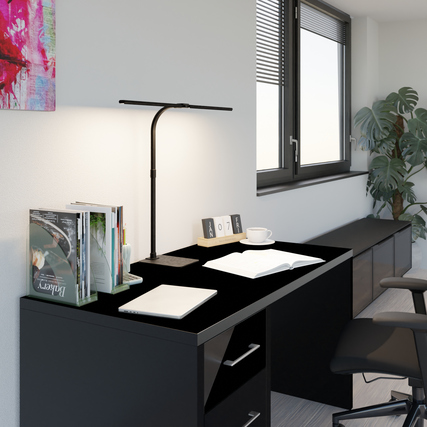 Tischleuchte im Wohnraum auf einem schwarzen Schreibtisch mit Dekorationsobjekten.