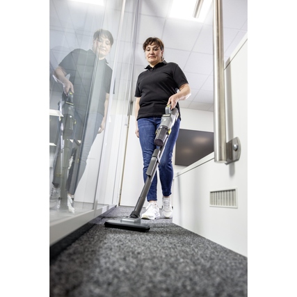 Person mit einem kabellosen Bodenstaubsauger reinigt einen Teppich im Büro.