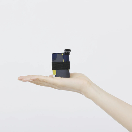 Gefaltete Shupatto Tragetasche in einer Hand, mit gehaltenem schwarz-gefühlt gebundenem Band.