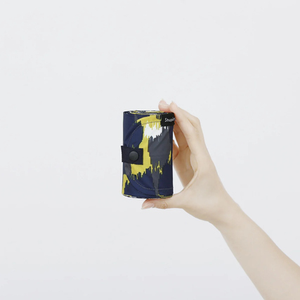 Händehaltende Person zeigt eine zusammengefaltete Shupatto Tragetasche in buntem Design.