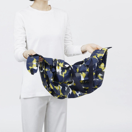 Eine Person zeigt eine gefaltete Shupatto Tragetasche in buntem, floralem Design.