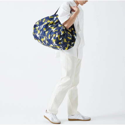 Mann trägt eine große, gemusterte Tragetasche über der Schulter in seitlicher Ansicht.