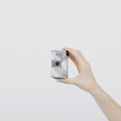 Hand hält eine gefaltete Shupatto Tragetasche im Design 'Floating Clouds' vor weißem Hintergrund.