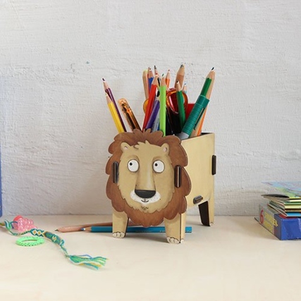 Holz-Stifteköcher in Form eines Löwen mit bunten Stiften im Inneren auf einem Schreibtisch.