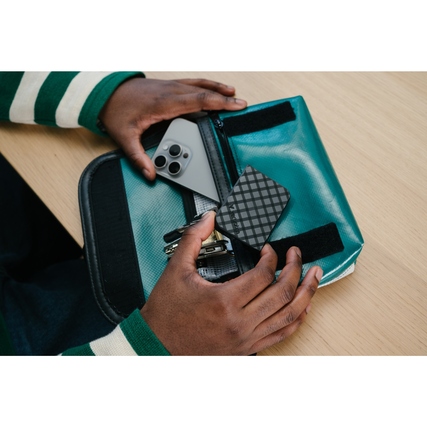 Externe SSD in einem tealfarbenen Tasche, neben einem Smartphone und anderen Gegenständen.