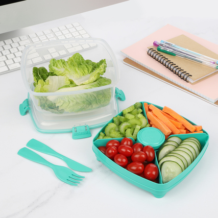 Bunte Salatschale mit verschiedenen Fächern für Gemüse und einem Dressingbecher, Besteck daneben.