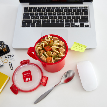 Rote Mikrowellensupptasse mit Eintopf, Laptop und Büromaterial auf einem Tisch.