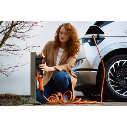 Frau kniet neben einem Elektroauto und hält ein orangenes Ladekabel in der Hand.