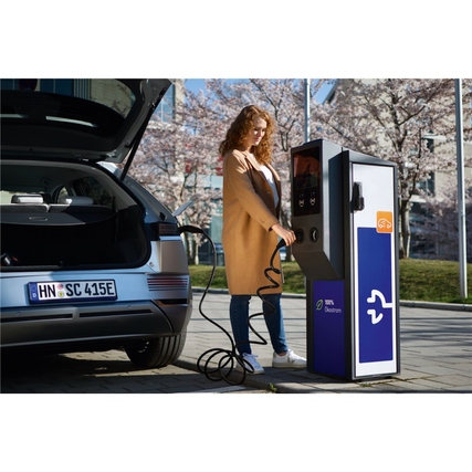 Frau lädt ein Elektroauto mit einem Ladekabel an einer öffentlichen Ladestation.