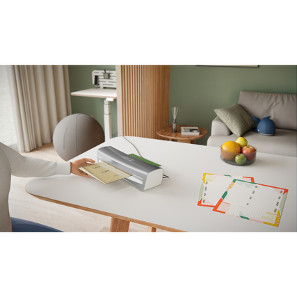 Laminiergerät in dunklem Grau auf einem Tisch mit Dokumenten und Zubehör im Hintergrund.