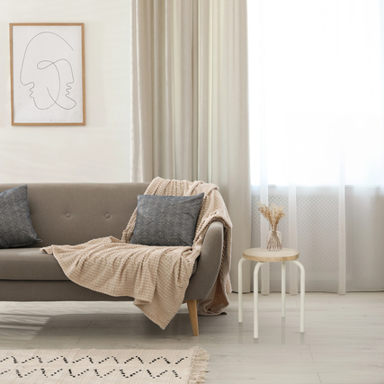 Sitzhocker im Skandi-Stil steht als Ablage neben einem Sofa in einer hellen, modernen Einrichtung.