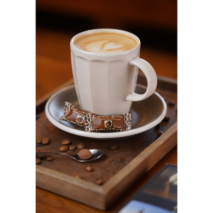 Tasse Kaffee auf einem Unterteller mit zwei Espresso-Bohnen in Zartbitter im Vordergrund.