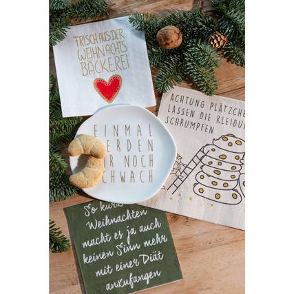 Porzellanteller mit goldener Schrift, umgeben von weihnachtlicher Dekoration und Gebäck.