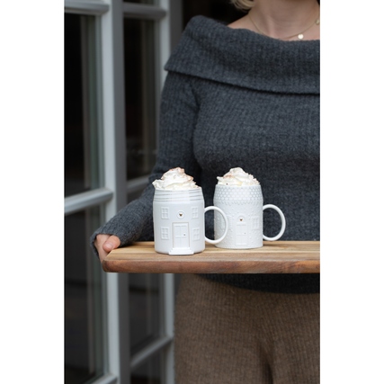 Zwei dekorative Tassen in Hausform mit Sahne, auf einem Holztablett in einer Personenas Hand.