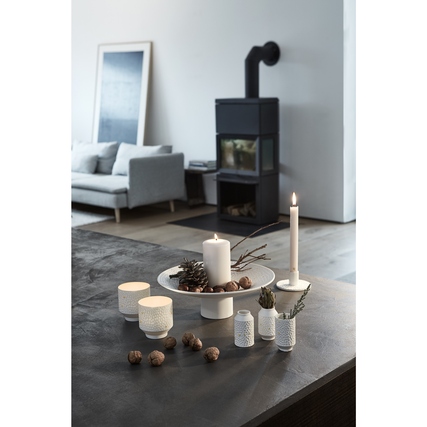 Porzellan-Windlicht in Sternschnuppenform auf einem Tisch mit Kerzen und Dekorationselementen.