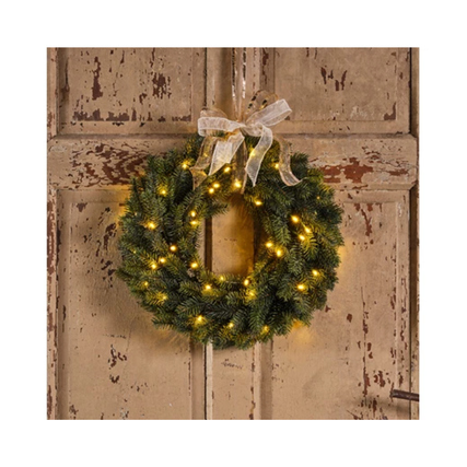 Grüner Weihnachtskranz mit Lichtern und Schleife an einer rustikalen Tür befestigt.