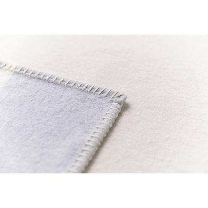 Detailansicht einer baumwollenen Decke mit Zierstichumrandung in hellen Farbtönen.