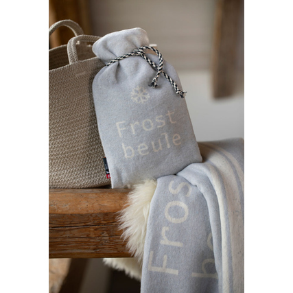 Grau gefärbte Wärmflaschenhülle mit Aufschrift "Frostbeule" auf einem Holzuntergrund.