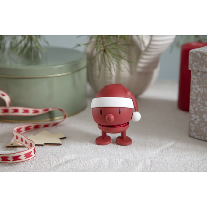 Dekorationsfigur in Form eines lächelnden, roten Weihnachtsmanns mit Mütze auf einem Tisch.
