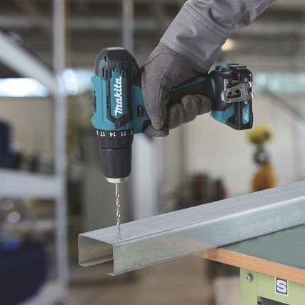 Makita Schlagbohrmaschine wird von einer Person mit Handschuhen über einem Metallstück gehalten.