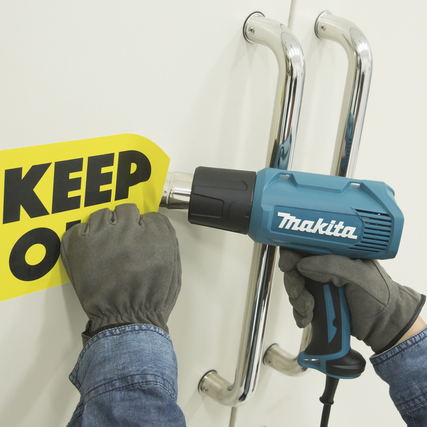 Makita Heißluftgebläse wird verwendet, um einen Aufkleber von einer Wand zu entfernen.